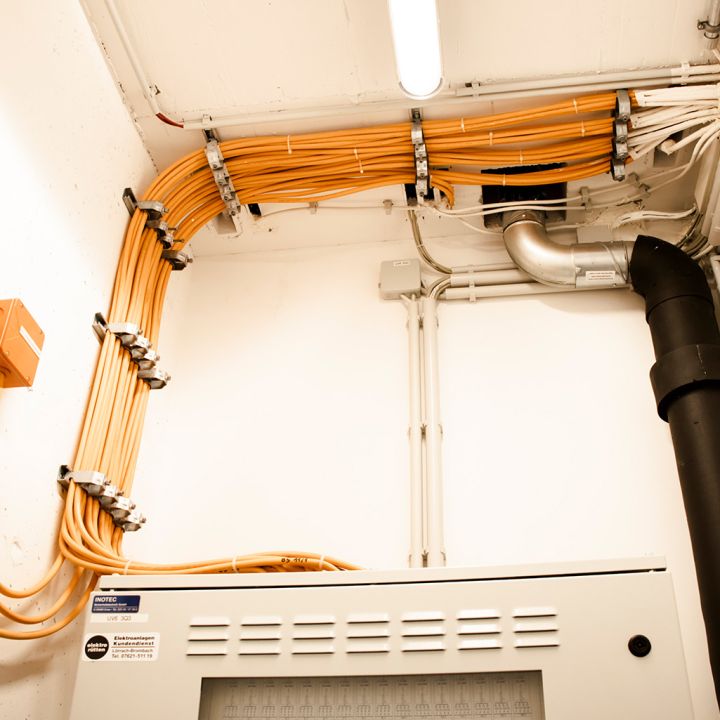 Viele orangefarbene Kabel verlaufen ordentlich an der Decke eines Technikraums.