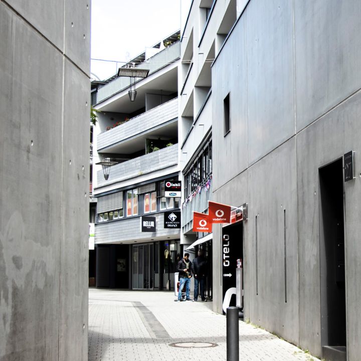Durch eine Gasse sieht man moderne Schilder und Eingänge verschiedener Geschäfte.