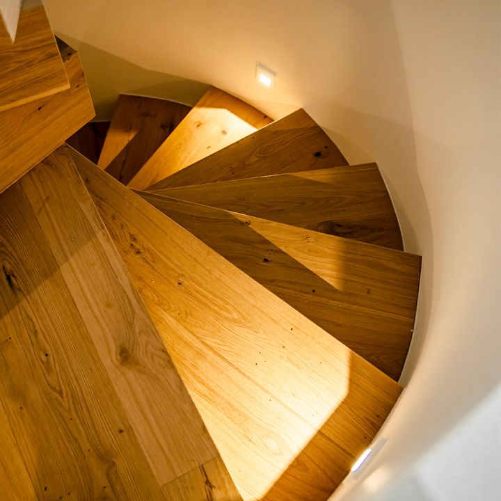 Eine Holz-Wendeltreppe wird durch kleine Treppenleuchten beleuchtet.