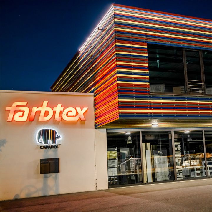 Farbtex-Geschäft mit bunter Fassade und beleuchtetem Firmenschild bei Nacht.