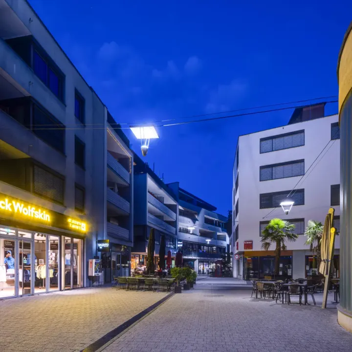 Eine moderne Einkaufsstraße wird am Abend von Straßenlaternen beleuchtet.
