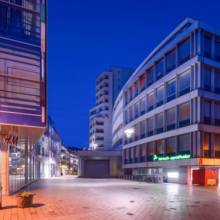 Moderne Gebäude und Geschäfte werden abends von Fassaden- und Straßenbeleuchtung erhellt.