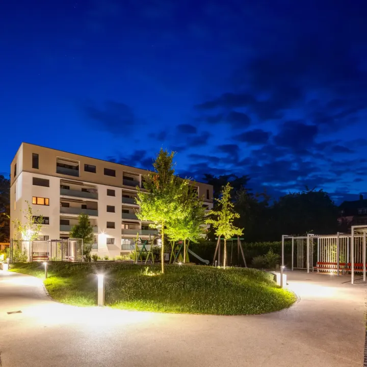 Eine Wohnanlage mit Wegen und Spielplatz ist nachts schön beleuchtet.