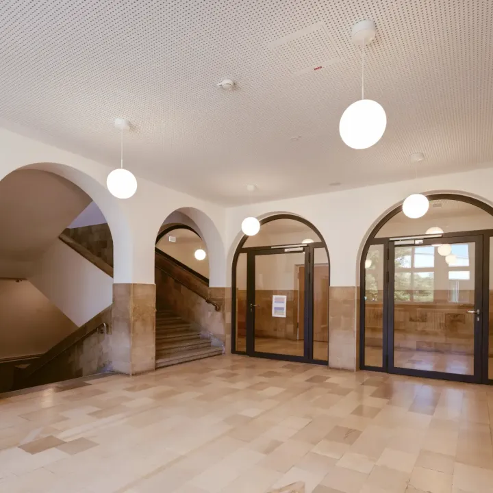 Ein Treppenhausfoyer in einem öffentlichen Gebäude mit großen, runden Hängelampen.