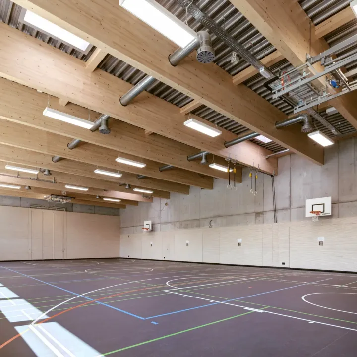 Große Turnhalle mit vielen Basketballkörben und Deckenleuchten.