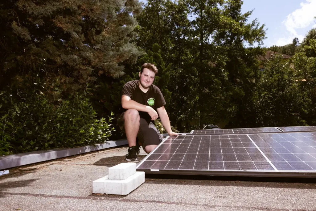 Ein Mitarbeiter kniet draußen neben installierten Solarmodulen auf einem Flachdach.