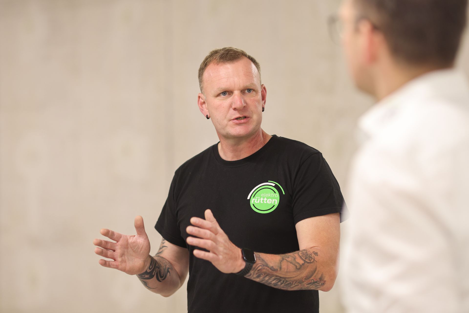 Eine Person im „elektro rütten“-Shirt spricht und gestikuliert beim Gespräch mit einer weiteren Person.