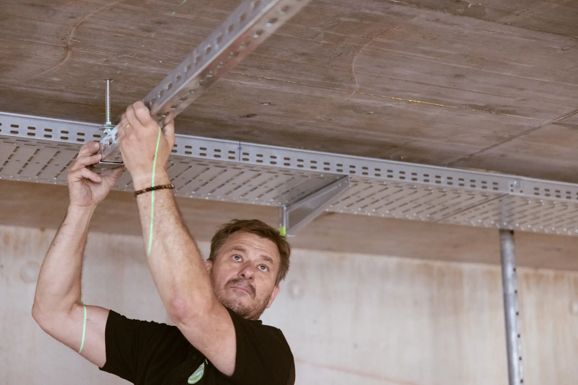 Ein Monteur befestigt eine Metallkonstruktion an der Decke einer Baustelle.